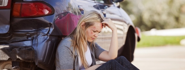 injured lady sitting beside car